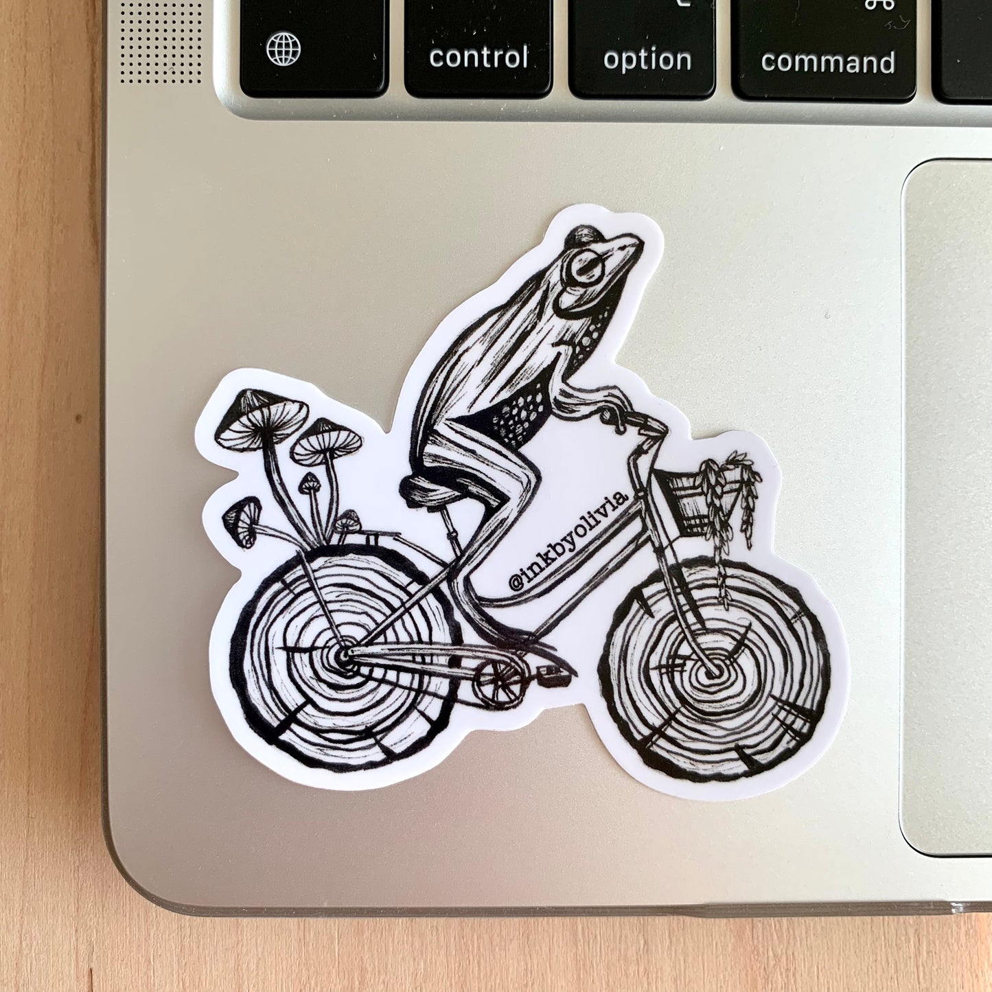 Hand-drawn frog riding a bike made of tree trunks, fun and whimsical design